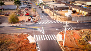 Vista aérea de sinalização viária em condomínio com organização de acesso a estacionamento, faixas de pedestres, pintura de solo e marcações de pare para segurança de veículos e pedestres.